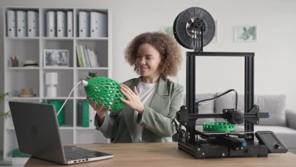 Portret van charmante creatieve vrouw met prototype van schaduw voor lamp in haar handen gedrukt op 3D-printer thuis, glimlachend en kijkend naar de camera — Stockvideo