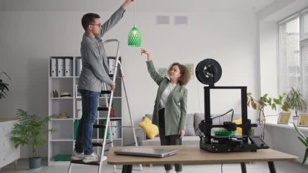 Tecnologias modernas, sala de arranjo jovem casal e pendura sombra lâmpada feita na impressora 3D em casa — Vídeo de Stock