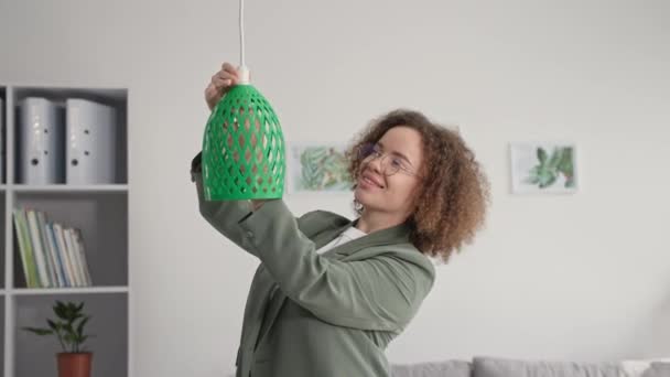 Moderne technologieën, jonge vrouw ontwerper is decoreren kamer en hangt 3D bedrukte lampenkap, glimlacht en kijkt naar de camera — Stockvideo