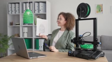 Akıllı genç bir kadın, evdeki 3D yazıcıda yazdırmak için bir bilgisayarda 3D model tasarımı yapmak için modern teknolojiyi kullanıyor.
