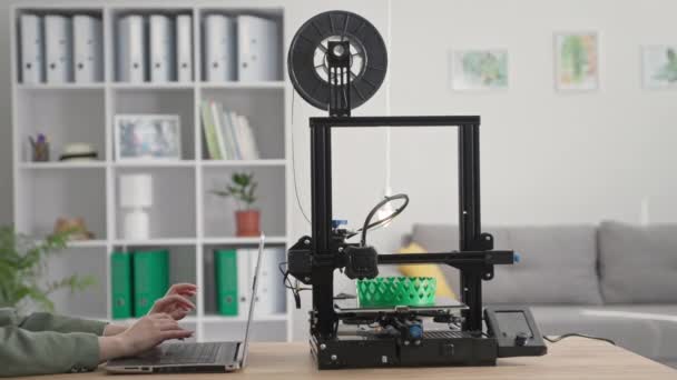Technologische vooruitgang, een jonge vrouw creëert een driedimensionaal model op een laptop computer tijdens het werken aan een 3D-printer thuis — Stockvideo