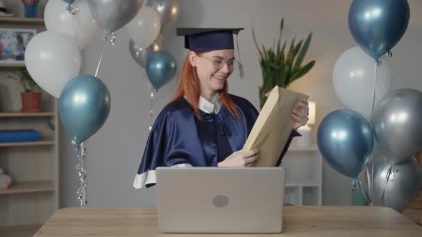 Virtual graduation and convocation ceremony, joyful young woman in mantle rejoices at presentation of diploma online using digital video communication technology on laptop while sitting at home in — Stock Video