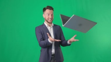 Çekici bir erkek işletme sahibinin portresi iş için dizüstü bilgisayarı yakalıyor gülümsüyor ve yeşil arka plandaki kameraya bakıyor, kroma anahtarı.