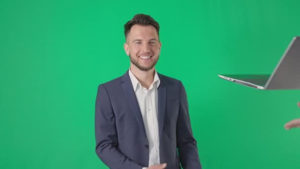 Бизнес-портрет, улыбающийся бизнесмен выпрямляет куртку и ловит ноутбук, улыбаясь и глядя на камеру на зеленом фоне — стоковое видео