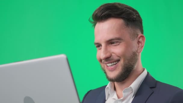 Retrato de negocios, joven hombre guapo sonriendo y trabajando en un ordenador portátil sobre un fondo clave de cromo verde, primer plano — Vídeos de Stock