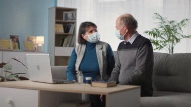 Modern tıp, tıbbi maskeli sağlıksız yaşlı erkek ve kadın karantina ve sosyal mesafe süresince laptoptan doktorlarla görüntülü konuşma yapıyorlar.