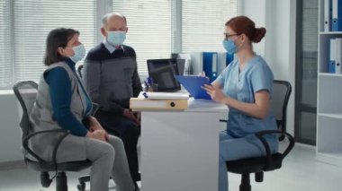 Sağlık hizmetleri, yaşlı bir adam ve yaşlı bir adam virüsü ve enfeksiyonu korumak için sağlık durumundan bahseden kadın doktorun resepsiyonunda tıbbi maske takıyor.