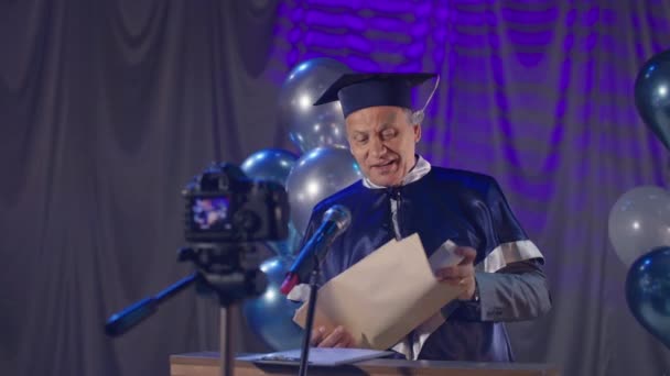 Samec rektor v plášti slavnostně provádí promoční ceremoniál pro absolventy vysokých škol s využitím moderních videokomunikačních technologií během karantény v důsledku koronaviru — Stock video