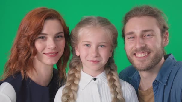 Vriendelijke familie, liefdevolle mam en pap kus op wang mooie dochter glimlach en kijk naar camera op groene achtergrond, chroom sleutel — Stockvideo