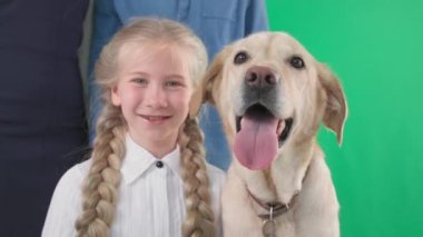 Mutlu bir çocukluk, köpeği ve ailesi olan sevimli küçük bir kız, yeşil arka planda gülümseyen ve kameraya bakan, krom anahtar.