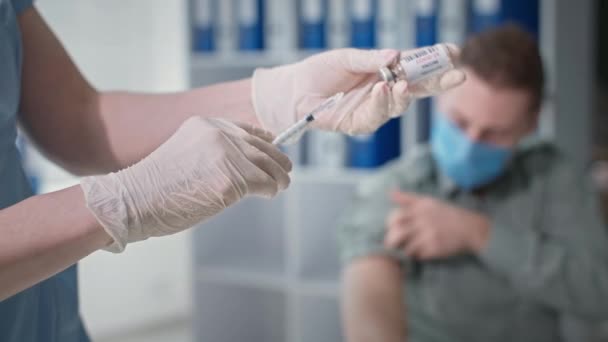 Junger Mann mit medizinischer Maske wird gegen Covid-19 geimpft, während er im Krankenzimmer sitzt — Stockvideo