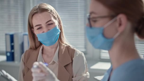 Γυναίκα που φοράει ιατρική μάσκα για την προστασία από τον ιό και τη μόλυνση υποβάλλεται σε εξέταση και μετρά τη θερμοκρασία με μη επαφή θερμόμετρο ραντεβού στο ιατρείο — Αρχείο Βίντεο