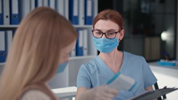 Femme médecin portant un masque médical et des gants examine le patient et mesure la température avec un thermomètre sans contact — Video