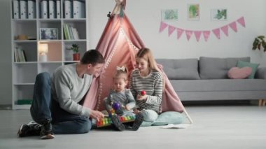 Çocukların yaratıcı gelişimi, sevgi dolu ebeveynler küçük bir kızla müzik aletleri çalarken odada büyük adamın arka planında oturup kameraya bakarken eğleniyorlar.