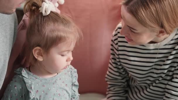 Alegre infancia, retrato de adorable niña con mamá y papá divirtiéndose juntos, mujer cariñosa besando a su hija con ternura y cuidado, primer plano — Vídeo de stock