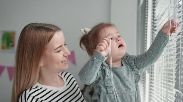 Mutterschaft, Porträt glücklicher weiblicher Eltern mit kleiner Tochter, die lächelt und gegen das Fenster in die Kamera blickt — Stockvideo
