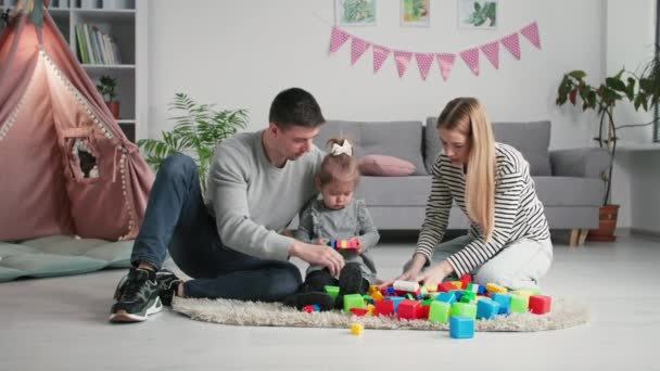 Juegos educativos, familia joven con niña jugar con la construcción de plástico multicolor conjunto mientras que pasar el rato en la habitación de los niños en el fondo wigwam — Vídeos de Stock