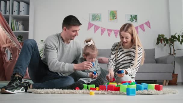 Rodiče-dítě vztah, mladý radostný manželský pár s malou dcerou bavte se těší hru v barevné ekologické plastové konstruktér při sezení v dětském pokoji — Stock video