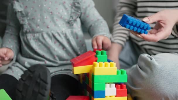 Lernspiele für Kinder, kleines Mädchen hat Spaß mit männlichen und weiblichen Eltern und sammelt farbige Plastikbaukästen, die im Raum auf dem Boden sitzen, Nahaufnahme — Stockvideo