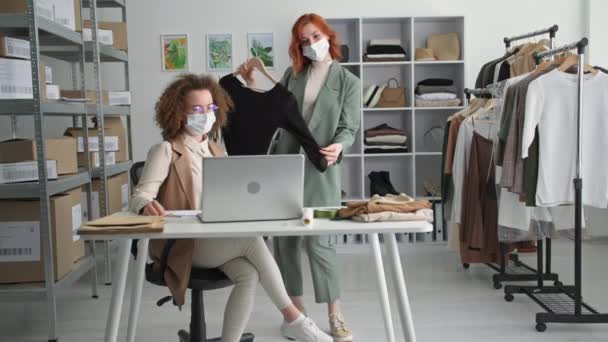 Онлайновая торговля, молодая рабочая группа в медицинских масках продают платья через интернет-чат с клиентом по видеосвязи на ноутбуке в магазине одежды — стоковое видео