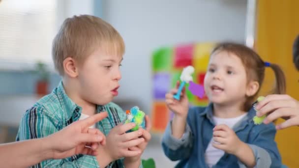 Дети с синдромом Дауна получают удовольствие на уроке педагогической терапии для детей с ограниченными возможностями в инклюзивной школе — стоковое видео
