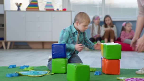 Potret anak kecil dengan sindrom bawah membangun menara bata berwarna selama kegiatan pendidikan untuk anak-anak — Stok Video