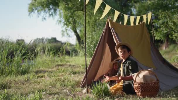 Kinder im Freien, süße kleine Jungen mit Sonnenhüten haben Spaß beim Tipi-Spielen in den Sommerferien außerhalb der Stadt — Stockvideo