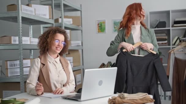 Okouzlující mladá žena prodává zboží přes internet pomocí video komunikace na notebooku, komunikuje se zákazníkem on-line, usmívá se a dívá se do kamery pozadí pracovní kolegyně — Stock video