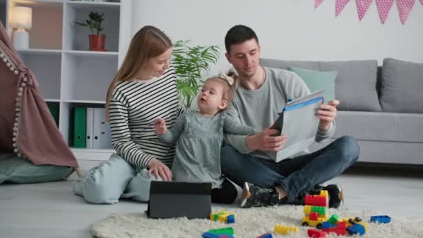 Día de los padres, hombre feliz con esposa e hijo pequeño femenino sosteniendo un regalo mientras se relaja con la familia en casa — Vídeos de Stock