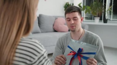 Evlilik ilişkisi, elinde hediyeyle neşeli bir adam karısını öper ve kucaklar, aile tatili sırasında karşılıklı anlayış ve desteğin tadını çıkarır.