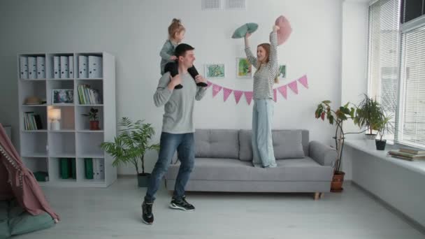 Allegra famiglia con bambino al collo si diverte a saltare sul divano durante una vacanza attiva a casa — Video Stock