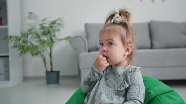 Comida para bebés, niña sana con apetito come uvas maduras dulces mientras está sentada en un sillón suave en la habitación — Vídeos de Stock