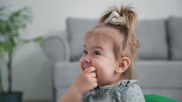 Glimlachend klein meisje met eetlust eet rijpe druiven voor snack en lacht terwijl zittend op de achtergrond van de bank in de woonkamer — Stockvideo