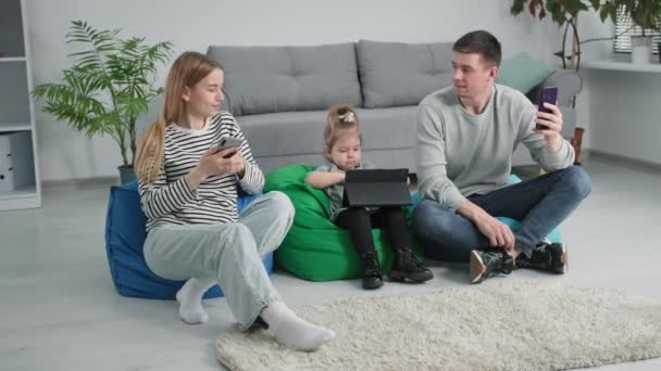 Foto familiar, hombre y mujer jóvenes y su hija pequeña utilizan los teléfonos inteligentes de tecnología moderna para y selfies mientras se relaja en casa — Vídeo de stock