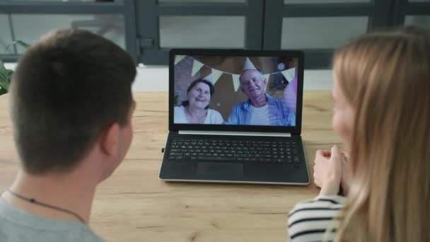 Távközlés, fiatal házaspár egy nő gyermek beszél videohívás egy laptop nagyszülők ül asztalnál otthon — Stock videók