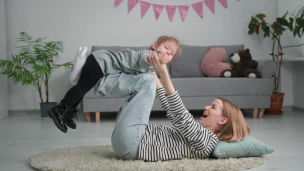 Niñez, niña alegre jugando con su madre feliz en el avión tumbado en el suelo en la sala de estar — Vídeos de Stock