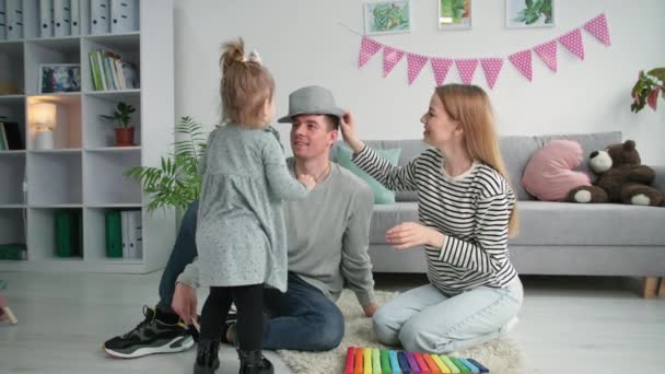 Gelukkig ouderschap, klein schattig meisje zet hoed op haar vader hoofd en kust hem tijdens familie tijd thuis — Stockvideo