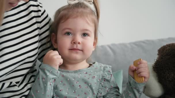 Attractive cute female child with cookies in hands sits in moms arms, smiles and looks at camera, close-up — Stock Video