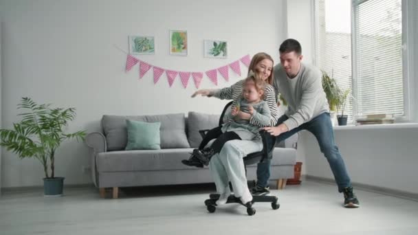 Семейные отношения, любящий отец весело прокатки жены и ребенка на стуле во время отдыха дома — стоковое видео