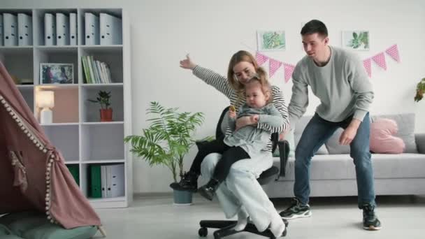 rodina zábava, radostný muž se baví válcování mladé ženy a dcery na židli, zatímco visí spolu doma