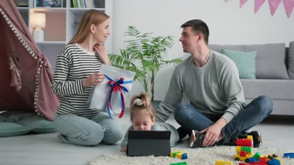 Jour des pères, femme aimante donne son mari présent tandis que l'enfant féminin joue sur tablette pendant les vacances en famille à la maison — Video