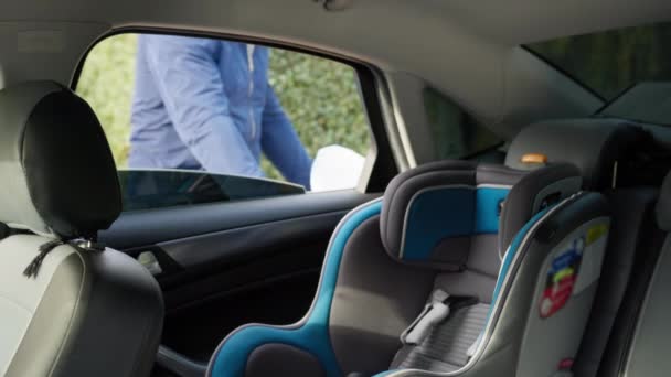 Paseo seguro, el padre pone al niño pequeño en el asiento trasero en el asiento del coche del bebé y abrocha los cinturones de seguridad durante el viaje conjunto con el niño — Vídeo de stock