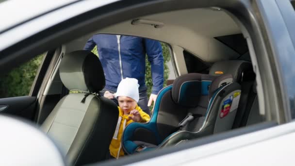 Bezpieczne dziecko, mężczyzna rodzic umieszcza syna na tylnym siedzeniu w foteliku samochodowym dziecka i zapiąć pasy bezpieczeństwa podczas wspólnej podróży z dzieckiem — Wideo stockowe