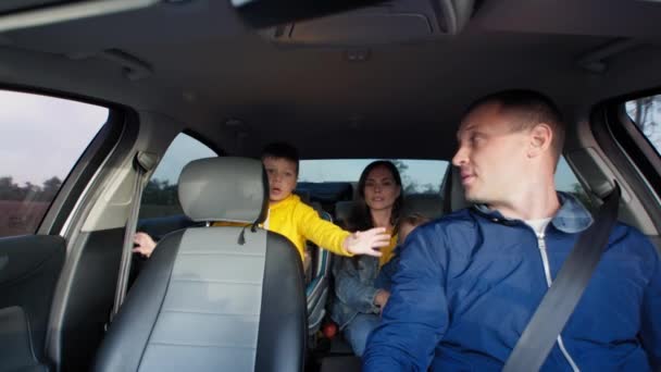 Homem dirigindo carro dirige sua amada esposa com bebê em seus braços com seu filho na cadeira de carro criança durante a viagem de fim de semana — Vídeo de Stock