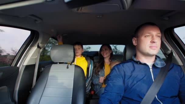 Alegre casal homem dirigindo e mulher no banco de trás do carro com crianças desfrutar de diversão passeio de piquenique — Vídeo de Stock