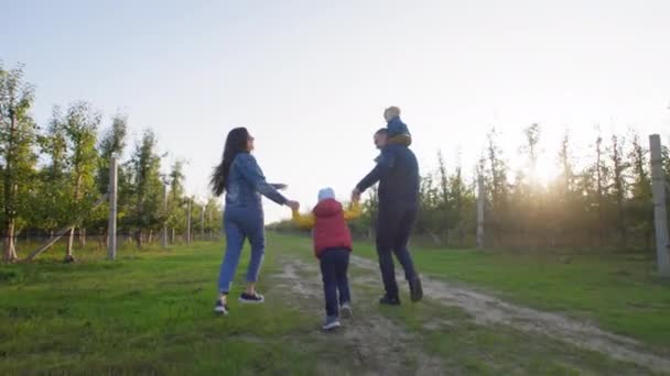 Rodiče a děti, máma a táta s dítětem kolem krku držet své syny za ruce a bavit se na venkově — Stock video