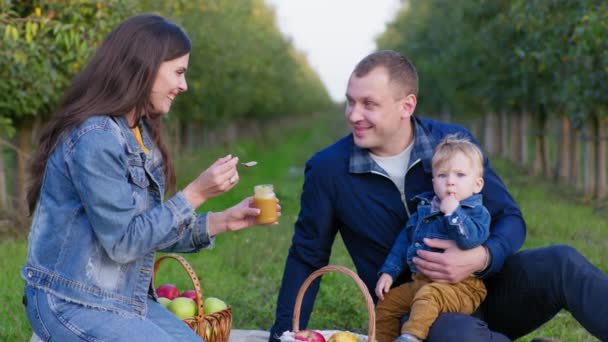 Дитяча їжа, мати годує маленького сина ложкою з фруктовим пюре в банку, сидячи в руках батьків — стокове відео