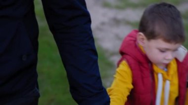 Ebeveyn desteği, parkta aile yürüyüşü sırasında babasının elini tutan mutlu çocuk portresi.