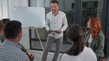 Genç ve başarılı erkek koç, başarı semineri sırasında grup seansı düzenler. El ele tutuşur, el ele tutuşur ve daire şeklinde otururken birbirlerini alkışlarlar.