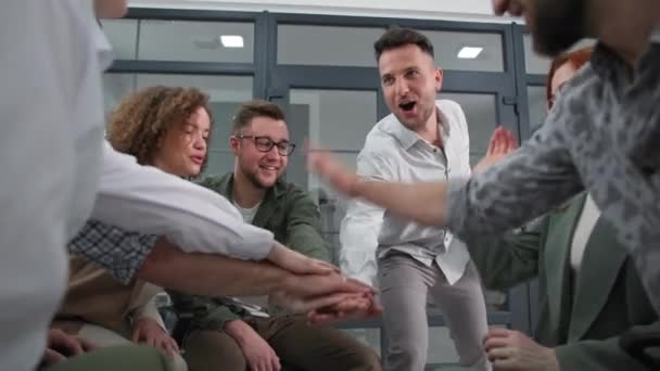 Поддержка, успешный мужской и женский коллектив складывает руки в круг поднимает и опускает, а затем хлопает, сидя в кругу во время мотивационной подготовки в офисе — стоковое видео